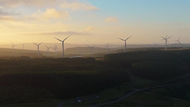 Soft Golden Hour Light Over Large Onshore Wind Farm with Road and Forest in South Wales Valleys.