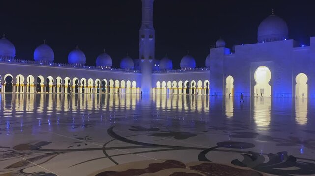 Grand courtyard of Sheikh Zayed Grand Mosque illuminated with dramatic blue lights