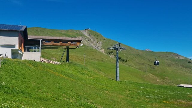 Summer view in Adelboden, Switzerland, focused on the Geils&ndash;Hahnenmoos gondola Bergstation rising above alpine meadows under clear Bernese Oberland skies