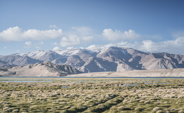Clear-water rivers and lakes in a mountain valley, pastures and green grassy fields set against mountain ranges and snow-capped, glacier-clad peaks&mdash;a scenic landscape background