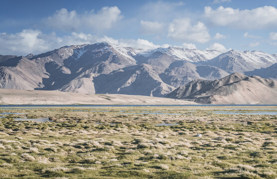 Clear-water rivers and lakes in a mountain valley, pastures and green grassy fields set against mountain ranges and snow-capped, glacier-clad peaks&mdash;a scenic landscape background
