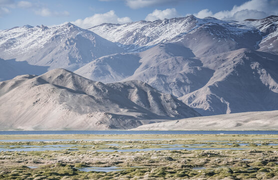 Clear-water rivers and lakes in a mountain valley, pastures and green grassy fields set against mountain ranges and snow-capped, glacier-clad peaks&mdash;a scenic landscape background