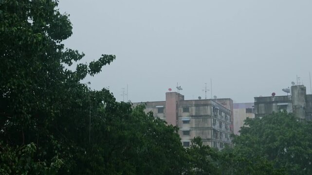 Stormy Monsoon Rain Over Old Residential Apartment Buildings with Satellite Dishes and Green Trees, Dark Gloomy Urban Cityscape
