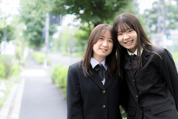 Fototapeta premium 屋外の緑背景で笑顔で寄り添う日本人女子高校生 二人で過ごす高校生活と青春のポートレート カメラ目線の笑顔