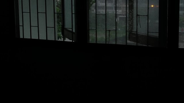 Dark Lonely Rainy Day View Through Old Window Bars with Rain Droplets, Melancholic Solitude Mood in Empty Dark Room Looking Out at Gray City, Bangkok Thailand