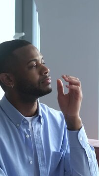 Pensive african american man sitting alone at home, looking out the window while lost in thought and contemplating his future, feeling a sense of loneliness, introspection, and solitude