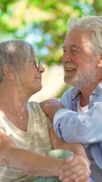 Beautiful senior couple sitting on a park bench, enjoying retirement together. The happy old man with a grey beard laughs and kisses his smiling wife, showing love and affection outdoors