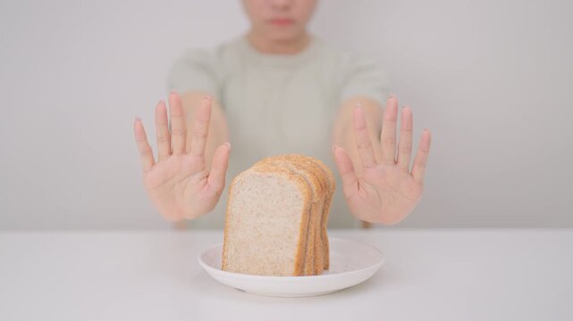 Unhappy woman showing Rejecting gesture and refusing to eat bread. concept of gluten intolerance, gluten sensitivity, carb loading concerns, or a disliking for unhealthy dietary habits