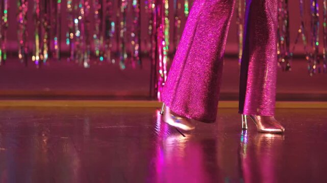 Disco dancer's sparkling purple flares and gold heels move to the beat against shimmering fringe backdrop.