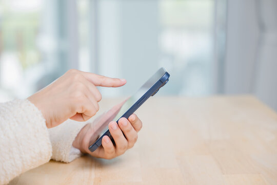 Female hands holding smartphone mobile phone using online technology on wooden table, tapping screen for social media communication, browsing internet, digital business lifestyle