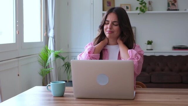 Overworked woman feeling tired and massaging her painful neck while working on a laptop from home, suffering from muscle strain and tension due to a sedentary lifestyle and bad posture