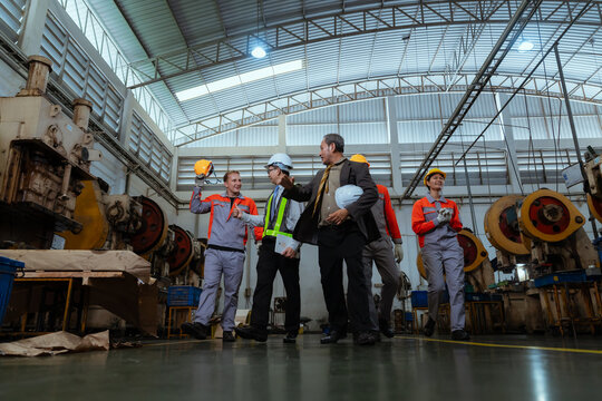 Workers and manager interact inside a factory during a team meeting in the afternoon while discussing performance and safety measures