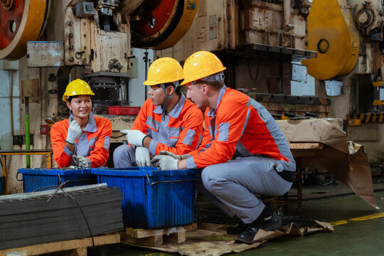 Workers are discussing tasks while sitting near blue containers in a factory