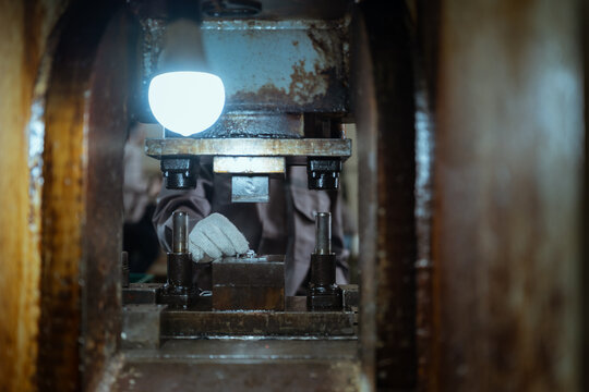 Worker operates machinery to shape metal in a workshop during evening hours with a focus on precise movements