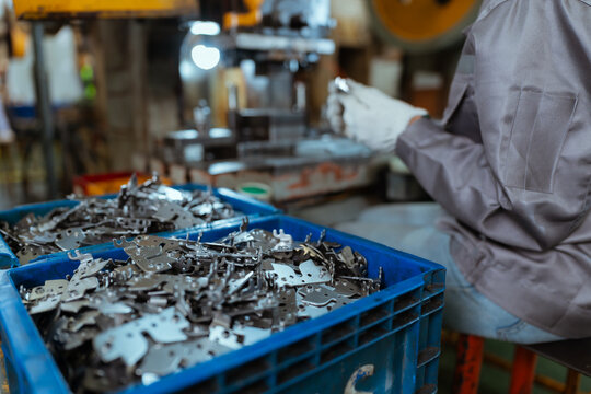 Workers handle metal parts in a factory during the daytime while sorting them in blue bins for further processing and assembly