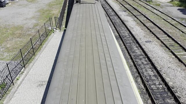 Top down view of a train car roof parked at the station platform with parallel rails.