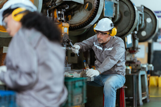 Workers use machinery in a factory to manufacture parts in a workshop during the day