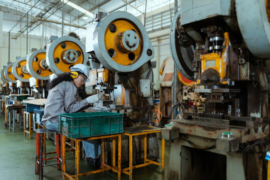 Workers operate machinery in a factory during daytime hours in a production setting with multiple workstations