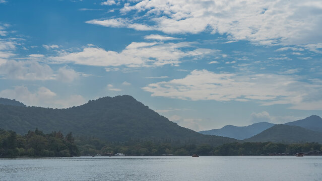 Boats sail on a beautiful calm urban lake. Mountains against a background of blue sky and clouds. China. Hangzhou. West Lake Xi Hu   