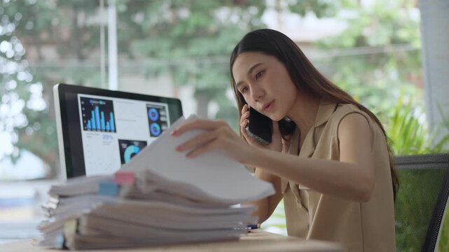 Stressed asian businesswoman managing paperwork and phone calls