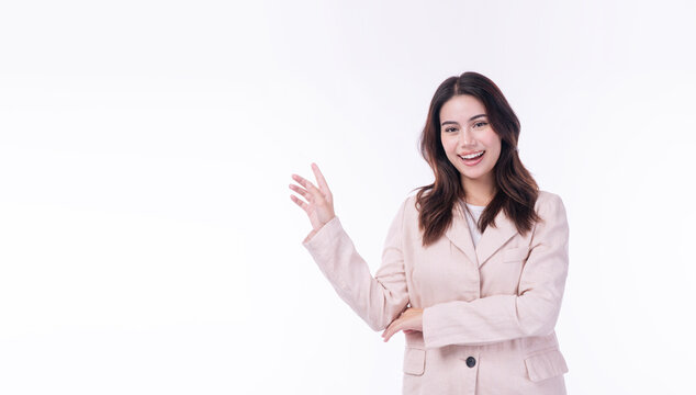 Smiling young Asian businesswoman in beige suit pointing hand at empty copy space on white background. Friendly female professional presenting product or recommending service corporate advertising.