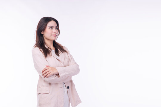 Confident young Asian businesswoman in beige suit with crossed arms looking away at empty copy space on white background. Professional female thinking about future corporate vision and success.