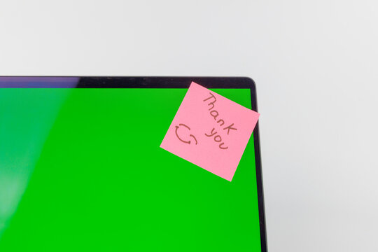 Close up view of a pink sticky note on a green chromakey computer screen showing the handwritten message thank you over white background