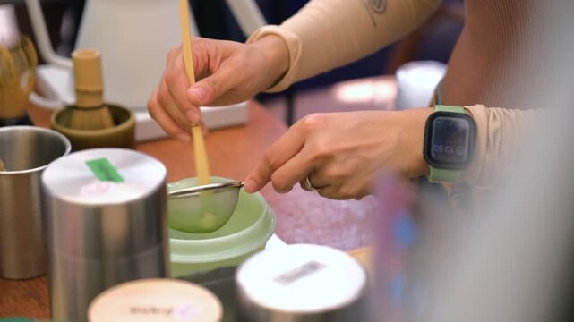 Close-up of a female vendor sifting bright green matcha powder through a fine mesh sieve during the traditional matcha tea preparation process