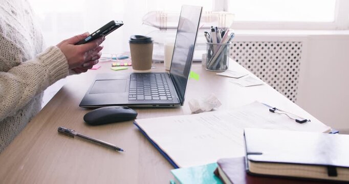 Laptop work. Freelance lifestyle. Unrecognizable woman manager using smartphone at office desk at professional workplace indoor.