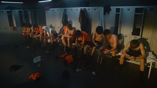 Youth Players Relaxing in Locker Room after Intense Training Session. Shirtless Teammates Sit on Bench Recovering, Checking Smartphones, and Enjoying Quiet Moment. Modern Sports Culture, Team Life.
