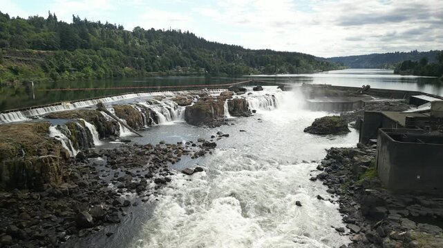 Aerial of tiered Willamette Falls and dam infrastructure in Oregon City with river flowing over multiple rock tiers and abandoned industrial buildings