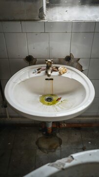 Old bathroom sink mounted on wall with damaged tile background and drain pipe