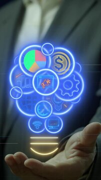 Open hand vertical shot holding glowing lightbulb filled with business data analytics icons. Creative cyber neon lighting background, integrated financial innovation and brainstorming concept.