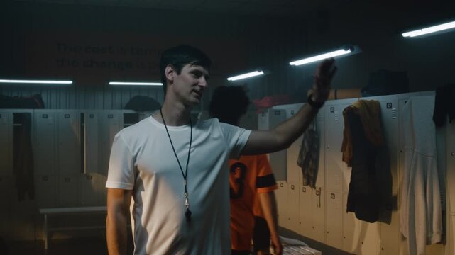 In Locker Room, Charismatic Coach in White T Shirt Performs Sequential Greeting Ritual With Youth Football Team. Team Bonding, Positive Reinforcement, Mutual Respect Between Mentor and Diverse Squad.