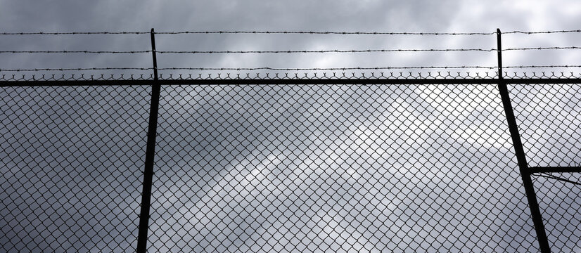 Barbed Wire Prison Fence Silhouetted Against Stormy Gray Sky