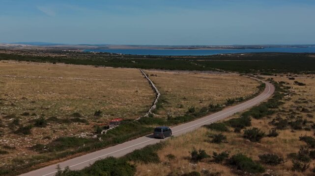 Silver van car driving past traditional stone walls and coastal fields on Pag Island, Croatia. Aerial