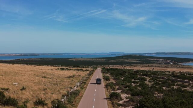 Camper van car driving down an empty country road through dry coastal landscape on Pag Island, Croatia.