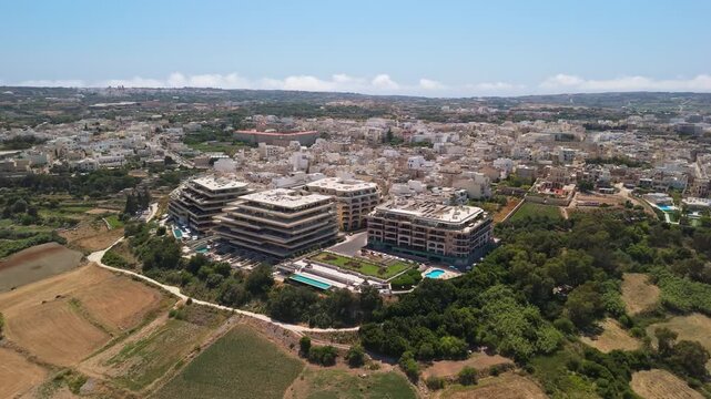Rabat, Malta apartment complex and hotel with pool, modern Mediterranean residential buildings, terraces and greenery in a suburban cityscape, captured by drone.