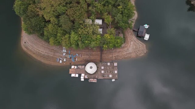 Lake Tarnița in Cluj County, Romania, with forested hills, shoreline piers, boats and lakeside buildings on the reservoir in the Apuseni Mountains, captured in a top down aerial view.