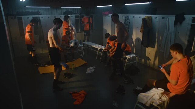 Youth Football Players Relaxing in Locker Room after Training Session. Teammates Change Clothes, Prepare For Shower, Chat About Practice, One Player Juggles Soccer Ball. Atmosphere of Amateur Sports.