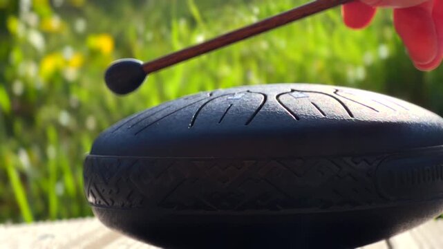 Handpan instrument produces soothing melodies in tranquil garden environment. Relaxation concept emphasizing the harmony of nature and music.