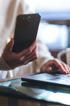 Vertical closeup image of a woman using smart phone and laptop computer in cafe