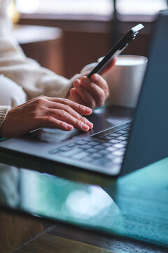 Vertical closeup image of a woman using smart phone and laptop computer in cafe