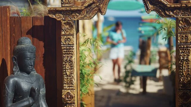 Ornate wooden entrance framing a blurred beach path leading toward turquoise umbrellas and the blue sea, creating an exotic coastal resort atmosphere