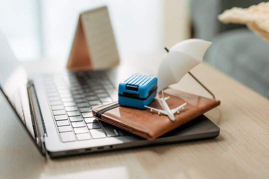 Miniature umbrella covering suitcase and airplane on laptop, concept of travel insurance, safe journey, and trip cancellation protection.