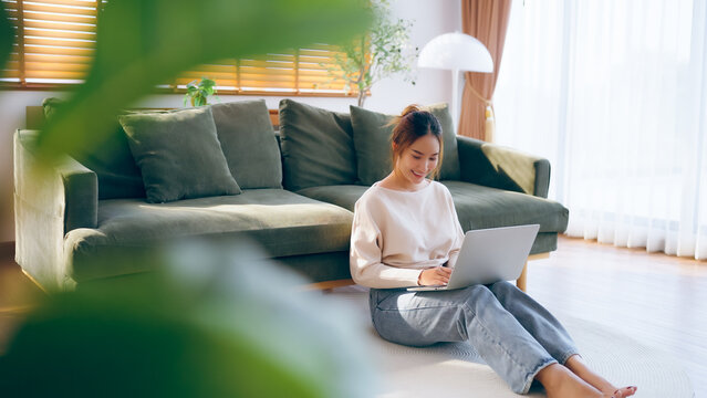 Young Asian beautiful woman relaxing on comfortable couch, using laptop at home, happy girl chatting with friends in social network, spending weekend, watching movie, shopping online