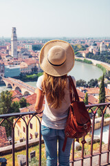 Fototapeta premium back view of woman tourist with straw hat and backpack looking at verona city view italy