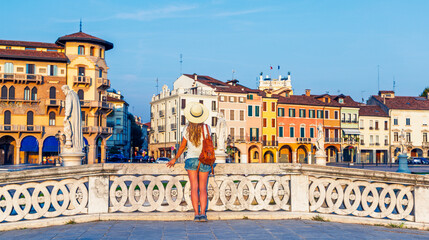 Fototapeta premium back view of woman traveler with backpack standing on bridge in prato della valle square padua, tour tourism in italy