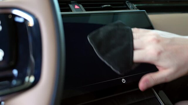 Male hand wipes the infotainment display inside a modern luxury car. Close-up of cleaning the touchscreen, removing dust and fingerprints while maintaining a spotless premium automotive interior.