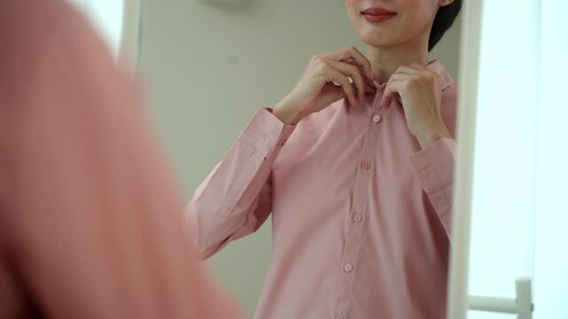 Close-up woman getting dressed in front of a mirror in a modern dressing room. Morning routine capsule wardrobe, personal styling, fashion confidence. Self-care and everyday lifestyle concept.
